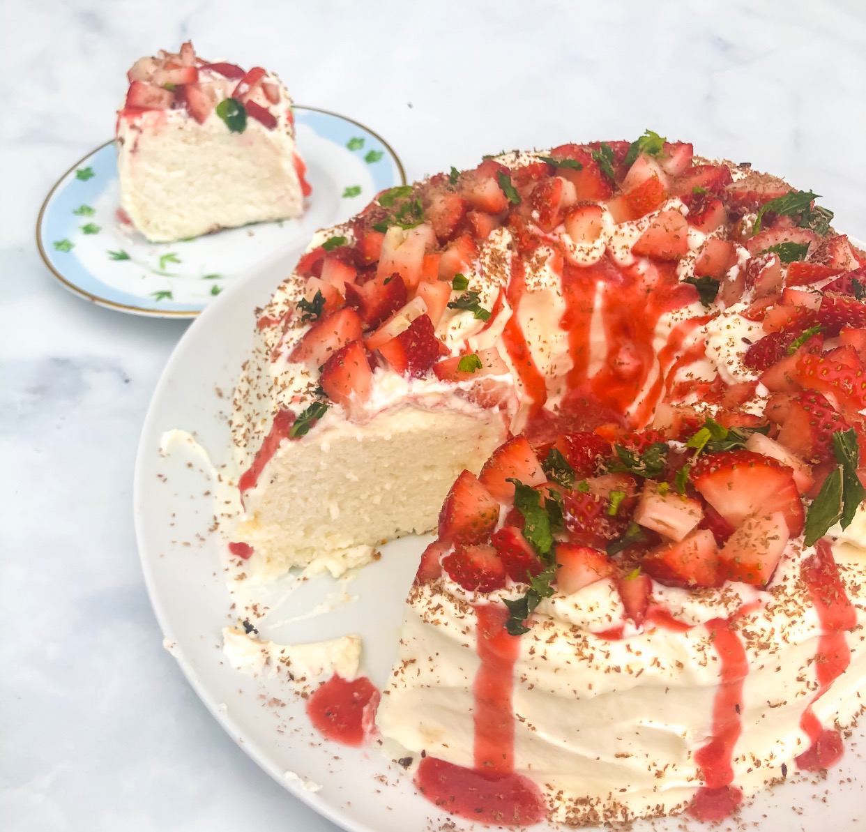 Finished gluten free angel food cake with whipped cream topped with strawberry compote, mint, and chocolate shavings